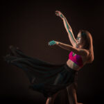 Young beautiful dancer in beige dress dancing on black background